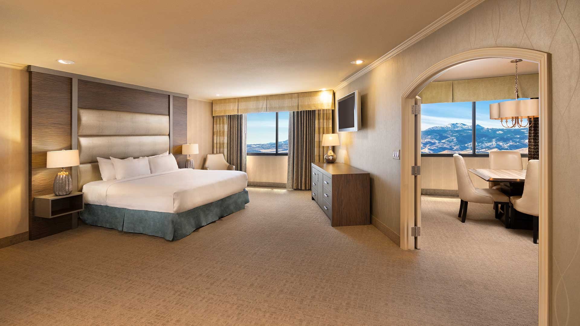 A wide view of a luxurious hotel suite with a large bed, separate dining area, and a mountain view.
