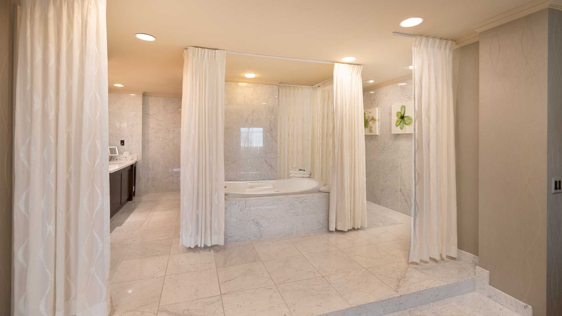 A luxurious bathroom with a large bathtub, marble tiles, and white curtains.