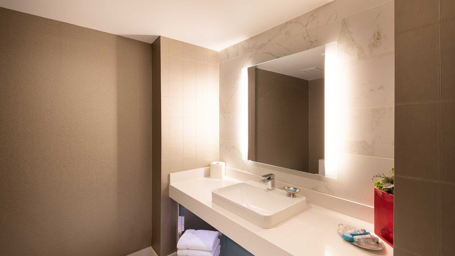 A clean bathroom with a white sink, mirror, and towels.