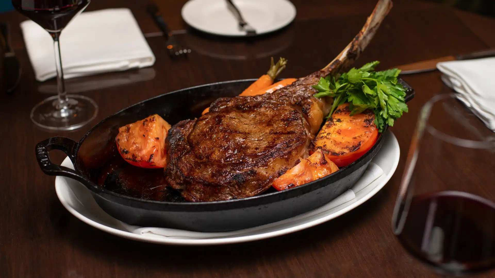a steak and vegetables in a cast iron pan on a table with wine