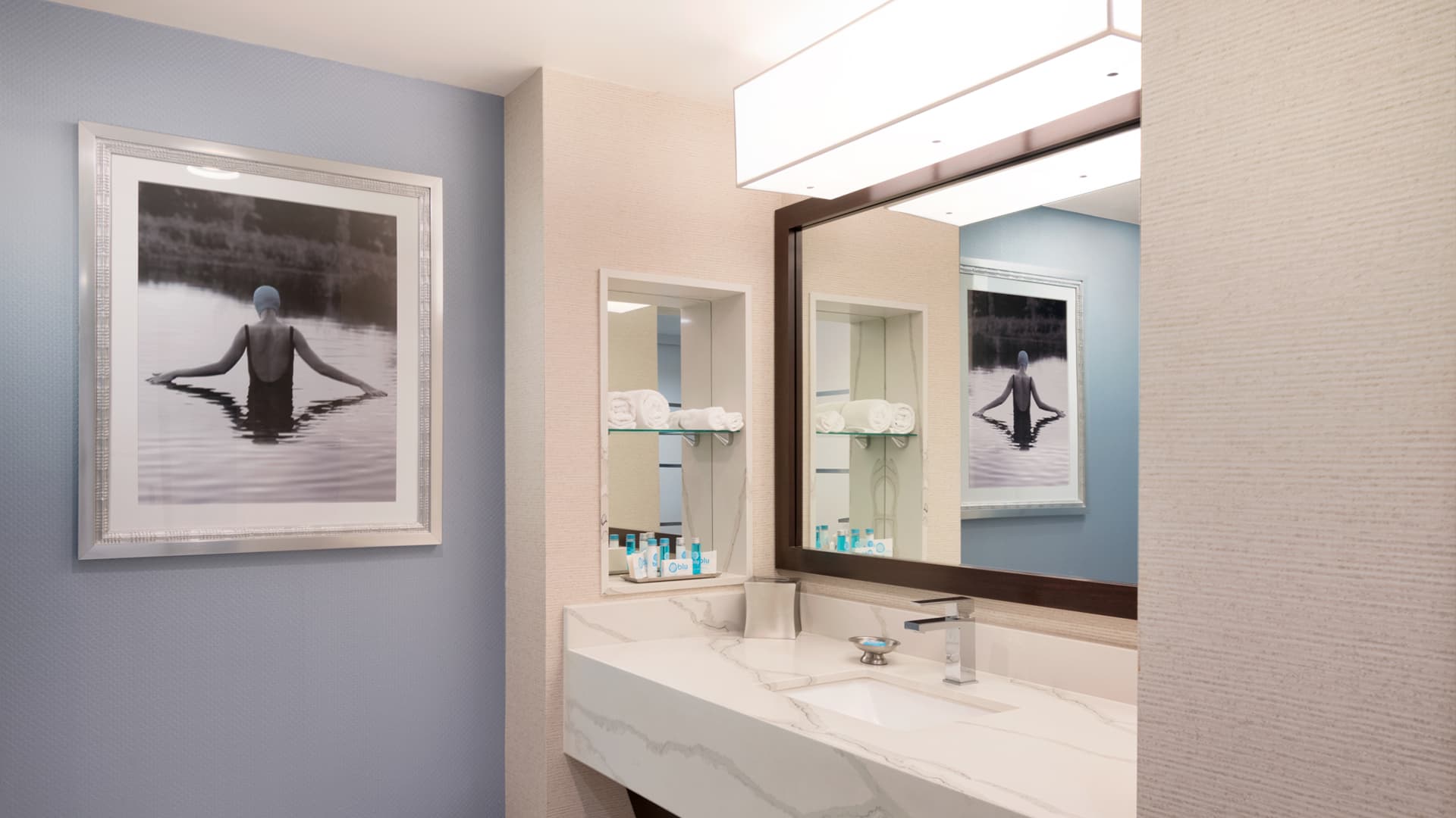 A bathroom sink area with a large mirror, marble countertop, and artwork on the wall.