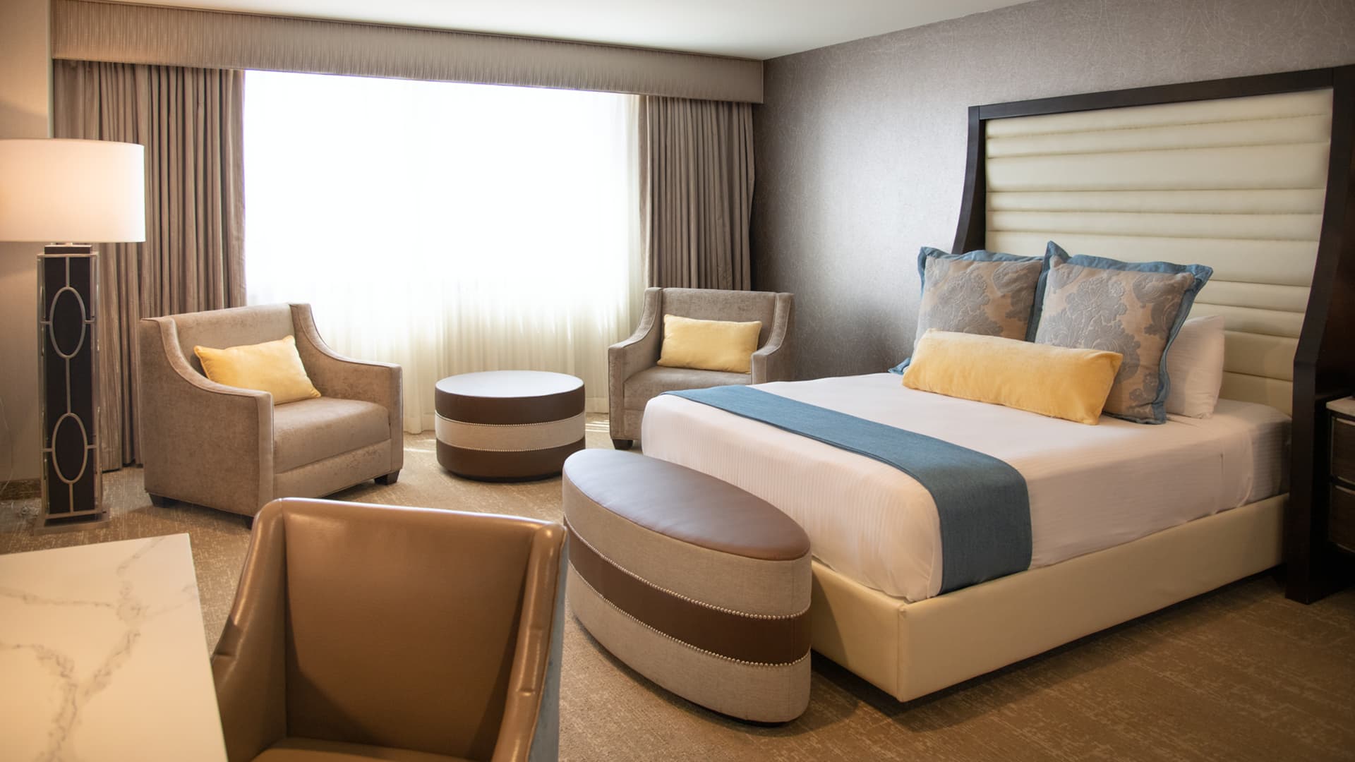 A hotel room with a king-size bed, seating area, and large window