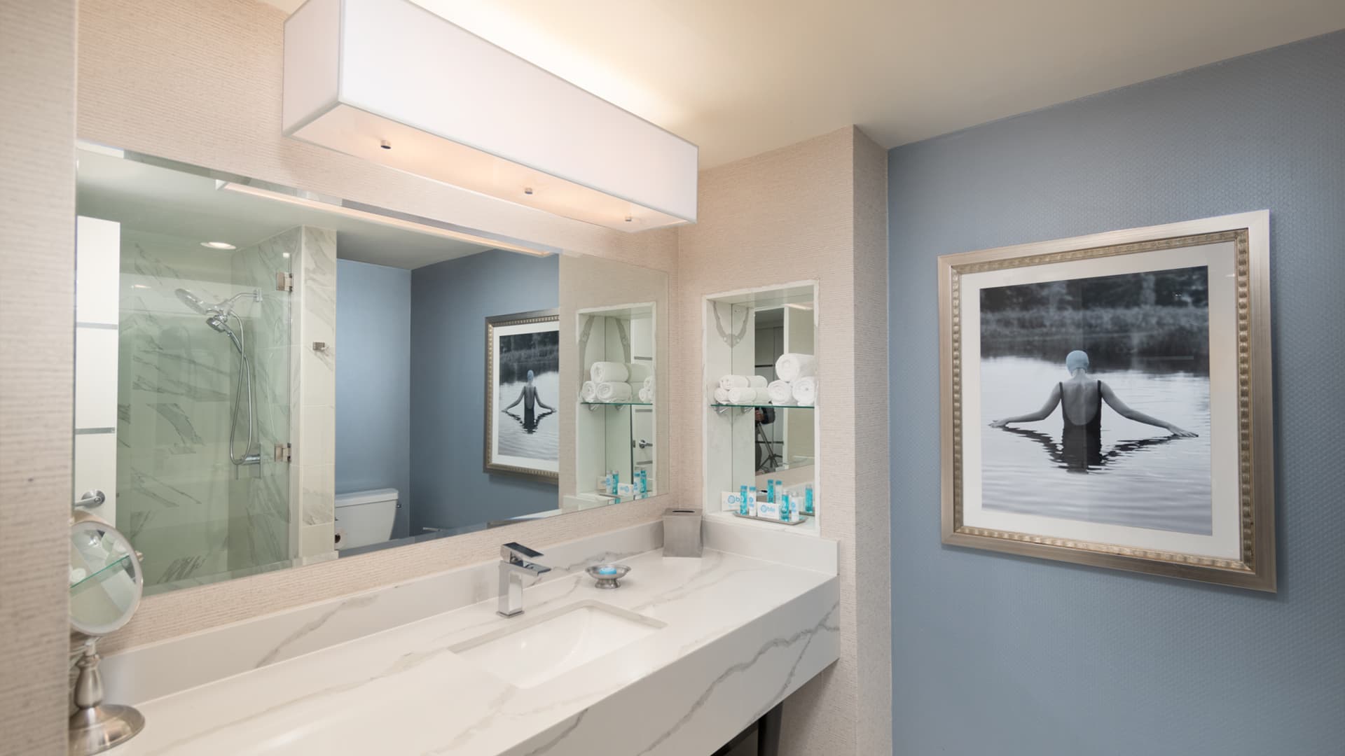 A bathroom with a large mirror, marble sink, and tiled shower with a glass door.