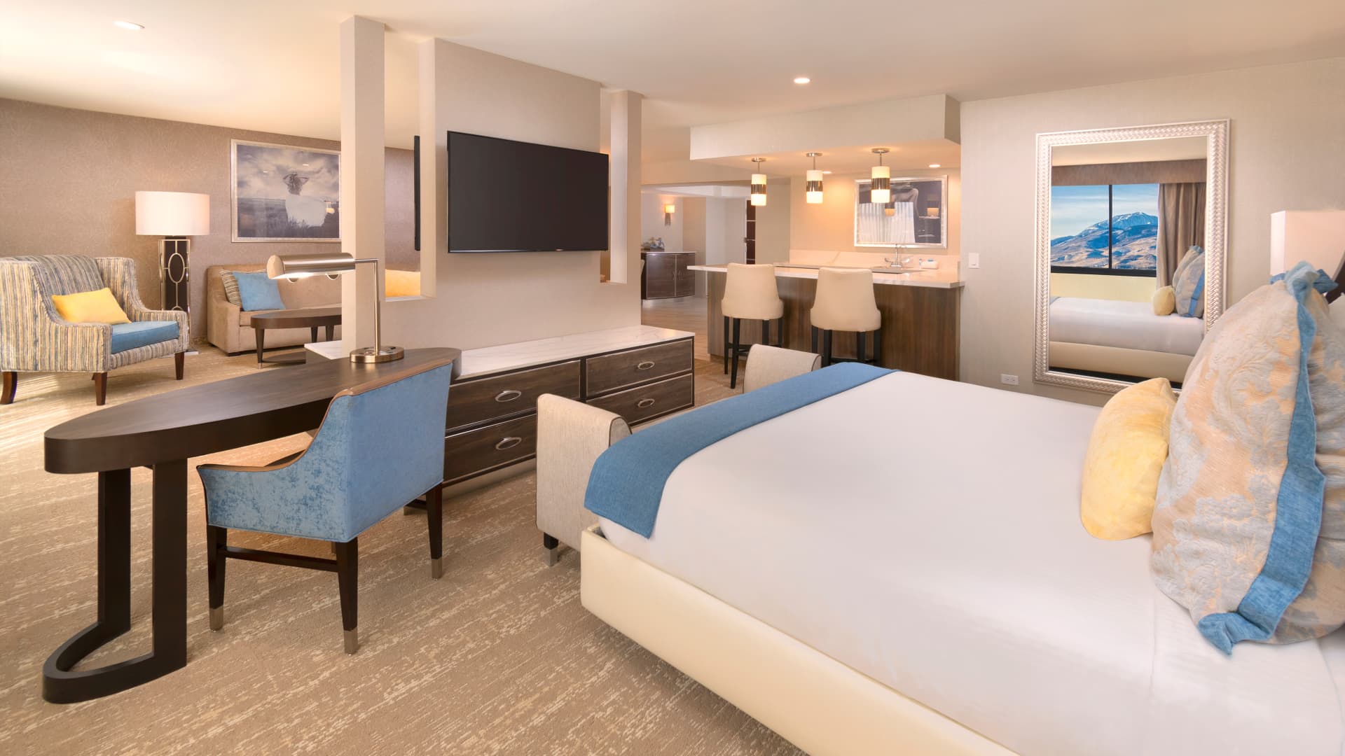A wide view of a hotel suite with a bed, desk, TV, and seating area.