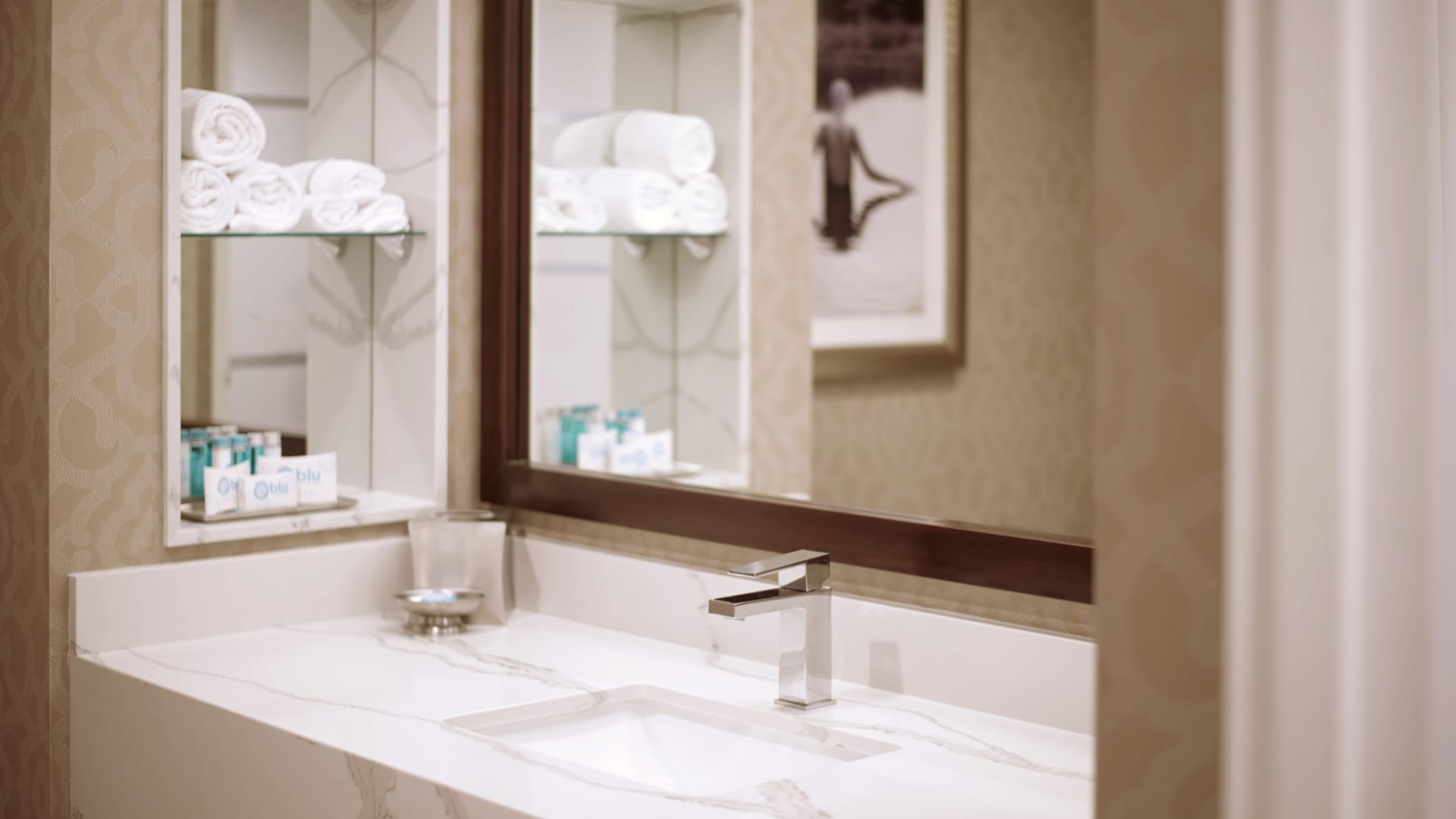 A bathroom sink area with a marble countertop, a large mirror, and amenities.