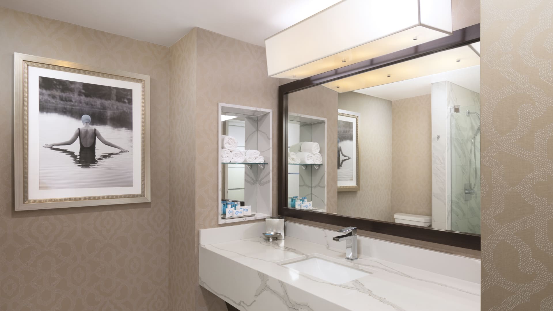 A bathroom with a large mirror, marble countertop, and artwork.