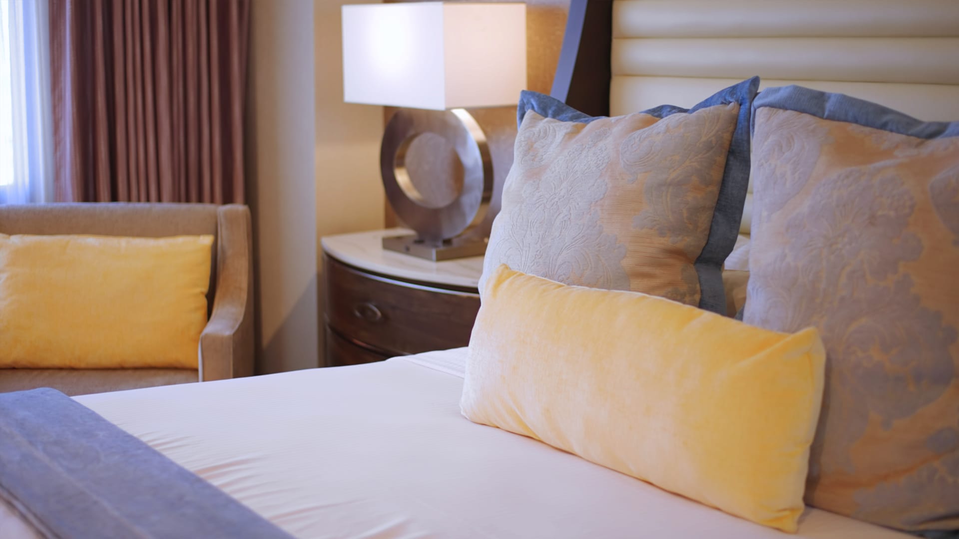 A close-up view of a bed with pillows and a lamp in the background.