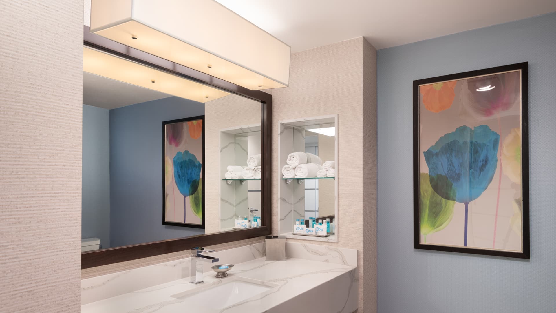 A bathroom with a large mirror, marble countertop, and artwork