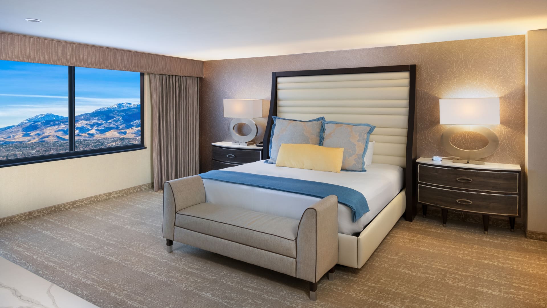 A hotel room with a large bed, two nightstands, and a window with a mountain view.
