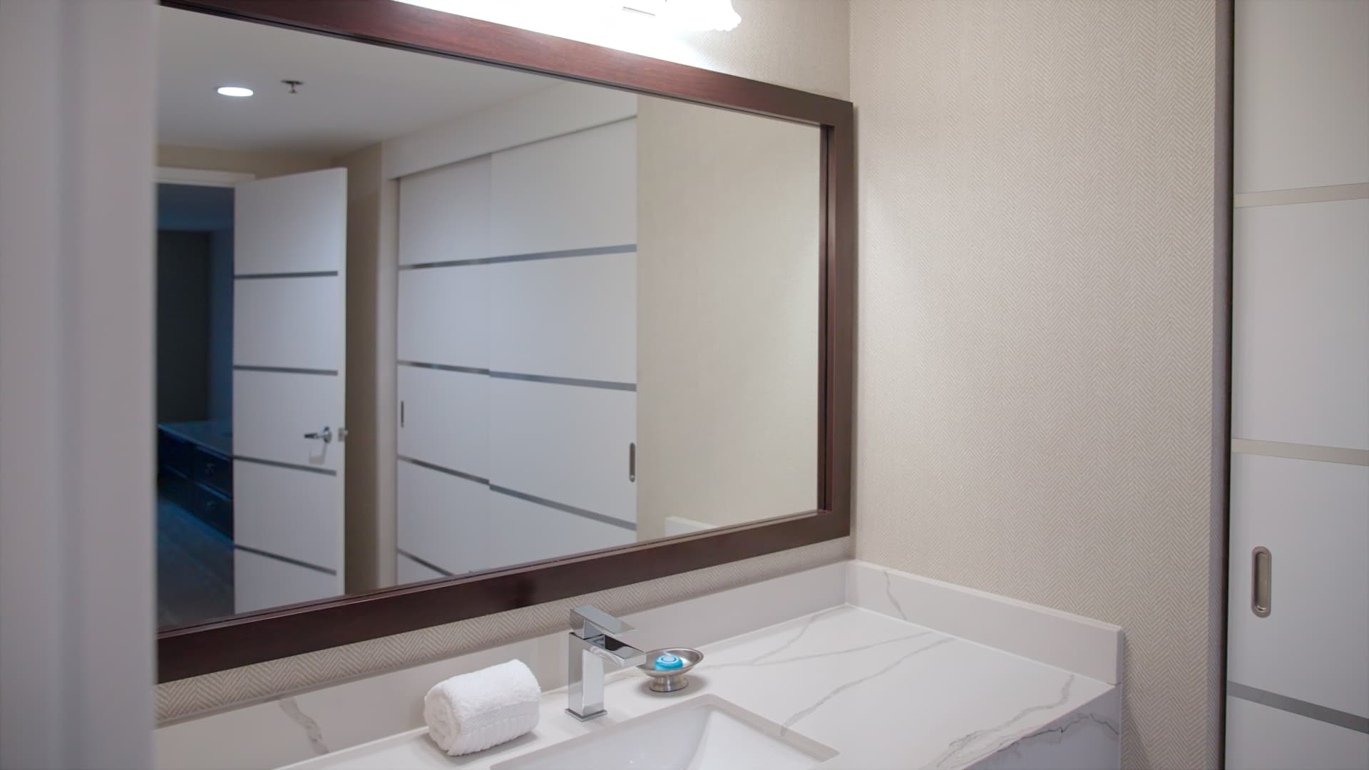 A bathroom sink with a large mirror, marble countertop, and silver faucet.