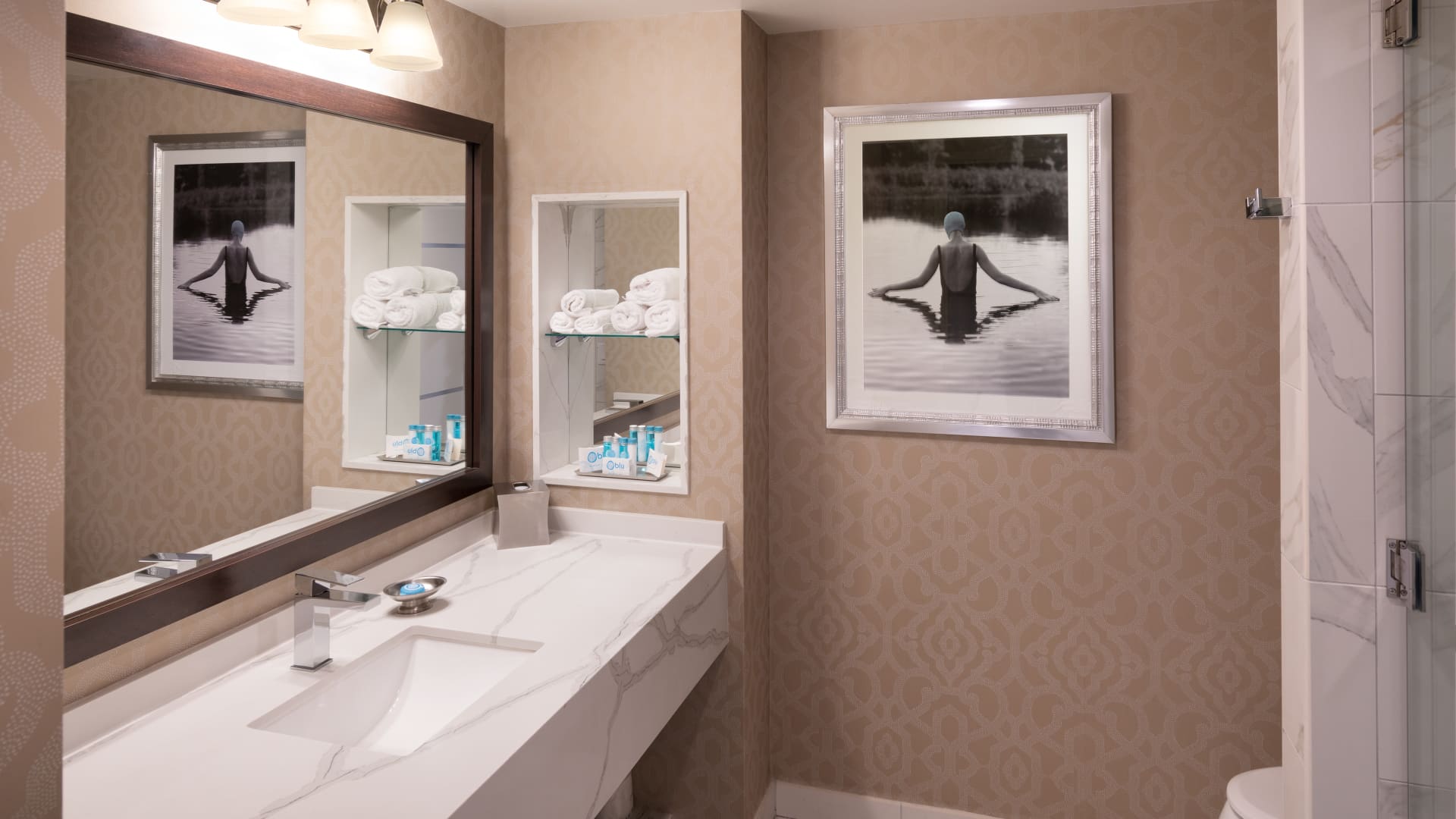 A bathroom with a large mirror, marble countertop, and tiled shower.