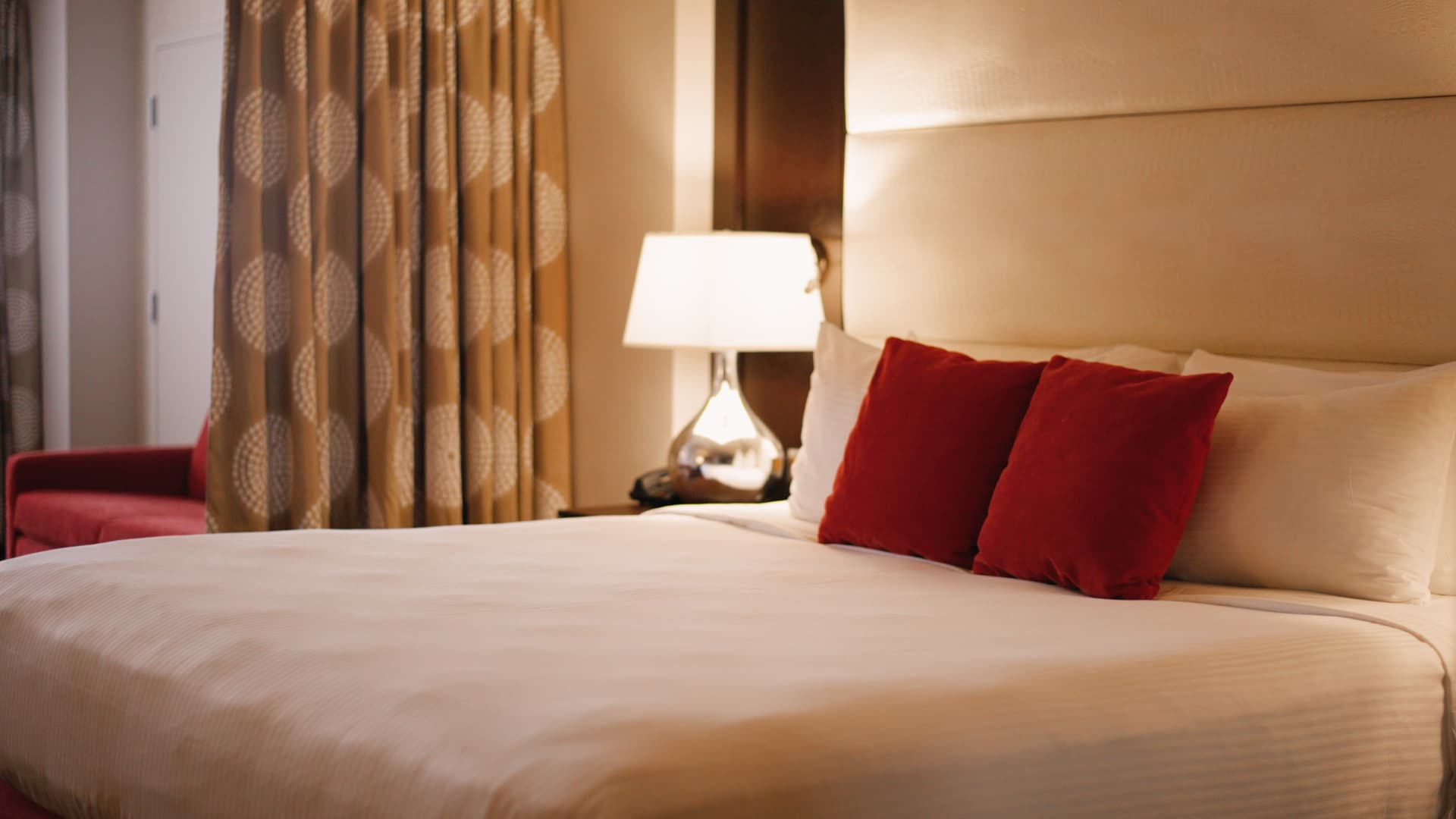 A hotel room bed with white sheets and red pillows