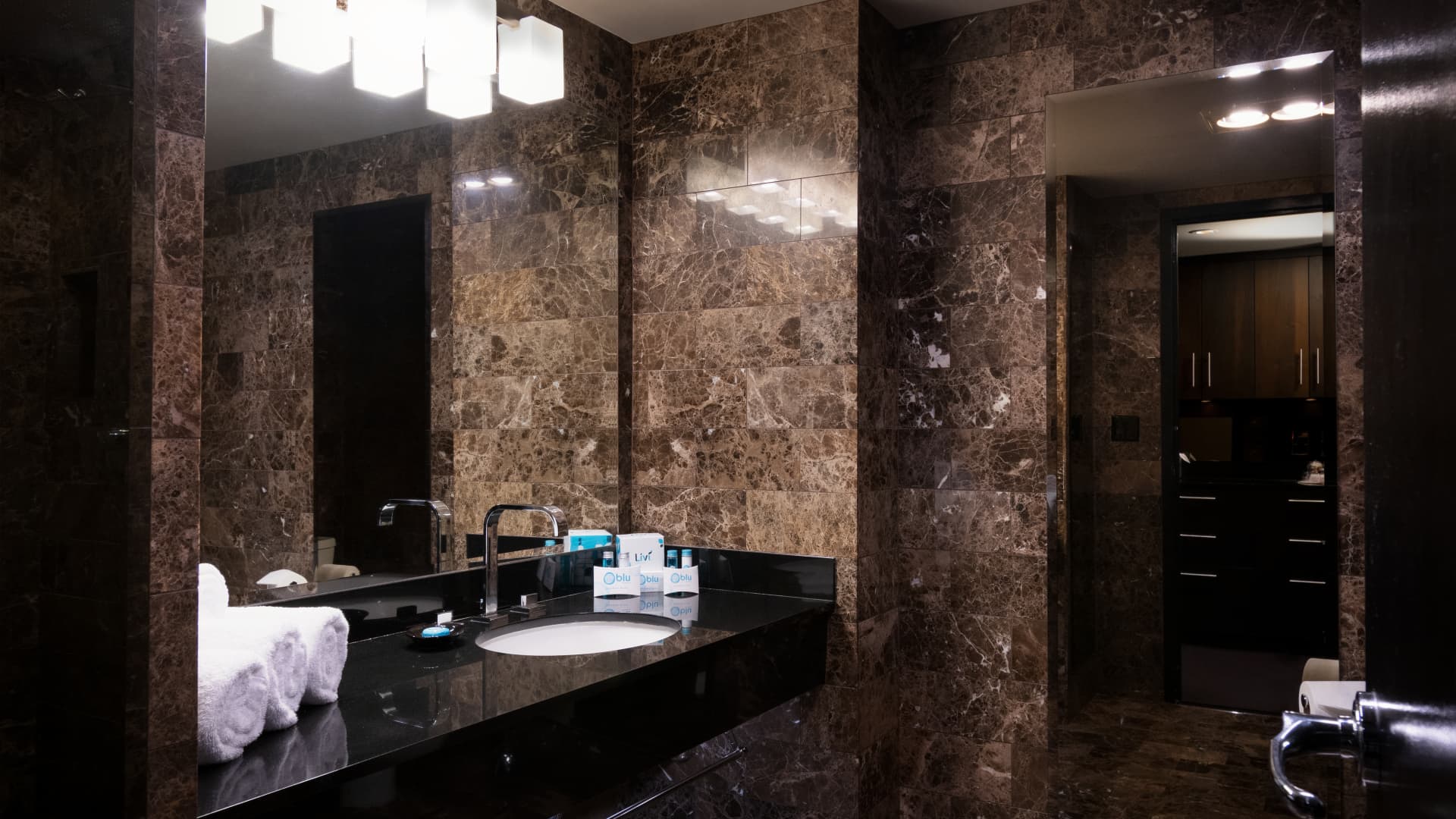 A luxurious bathroom with marble walls, a black countertop, and a large mirror.