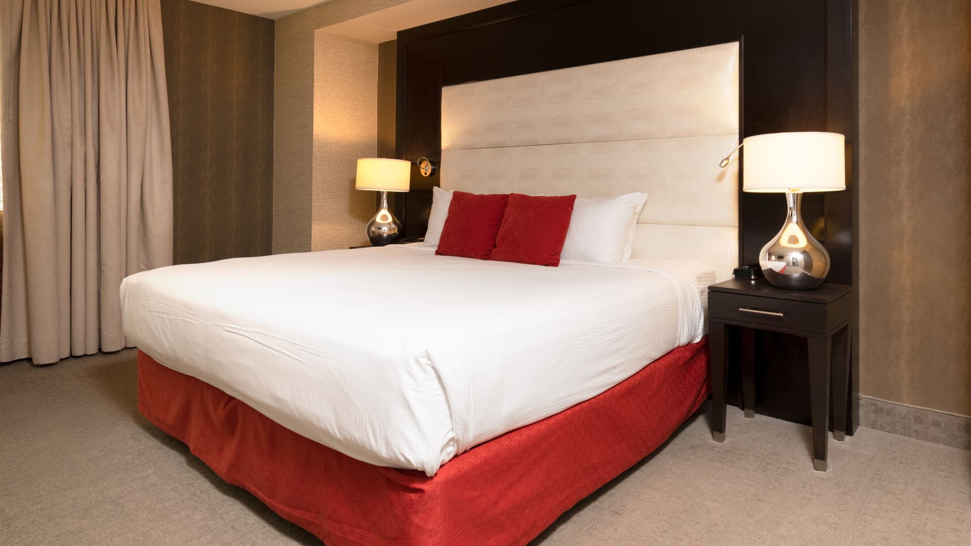 A hotel room with a large bed, two nightstands, and a window with curtains.
