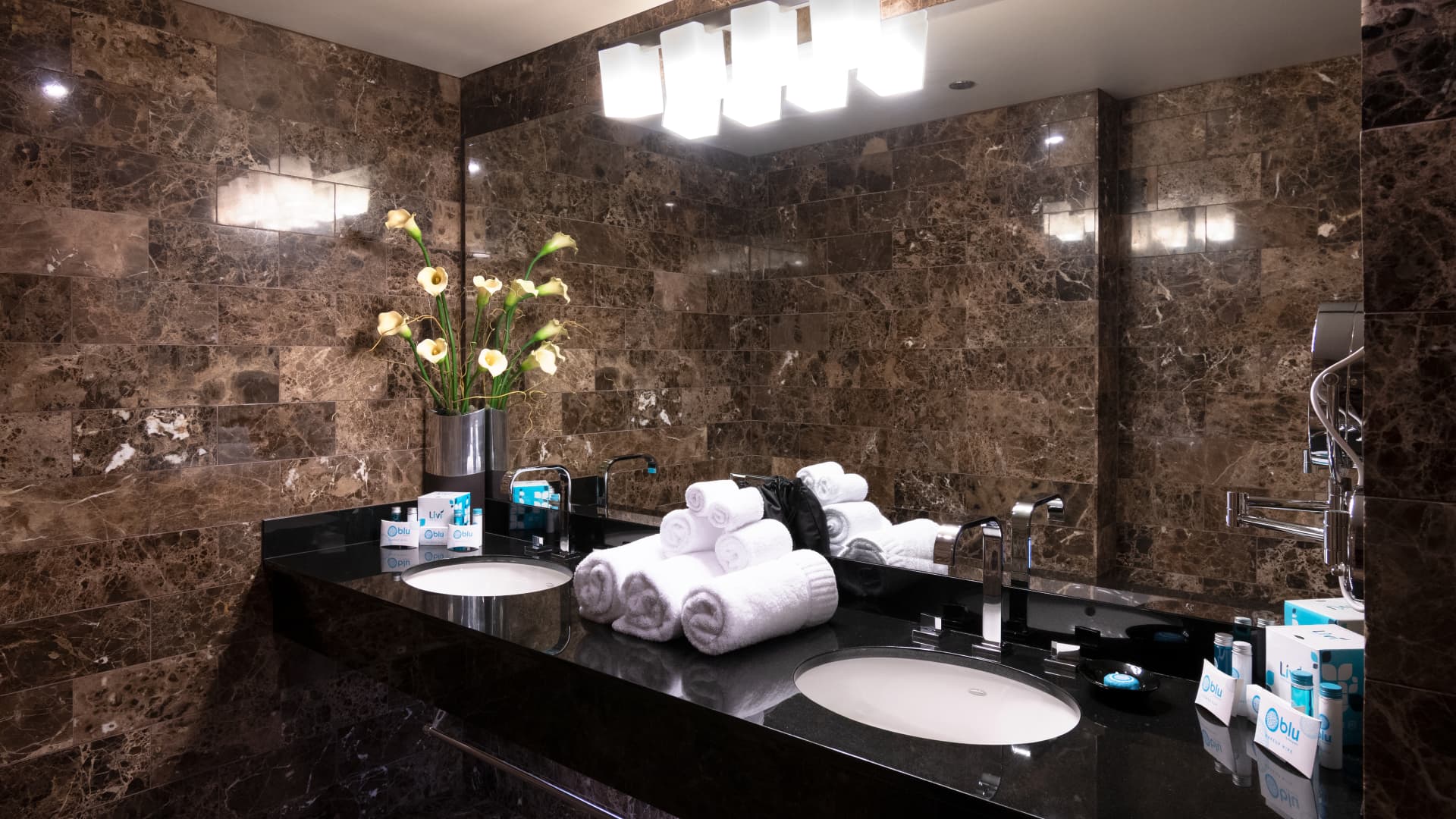 A luxurious bathroom with a double vanity, marble walls, and amenities.