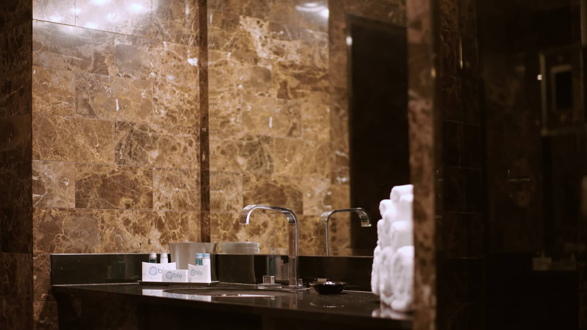 A bathroom sink with a marble wall, mirror, and amenities.