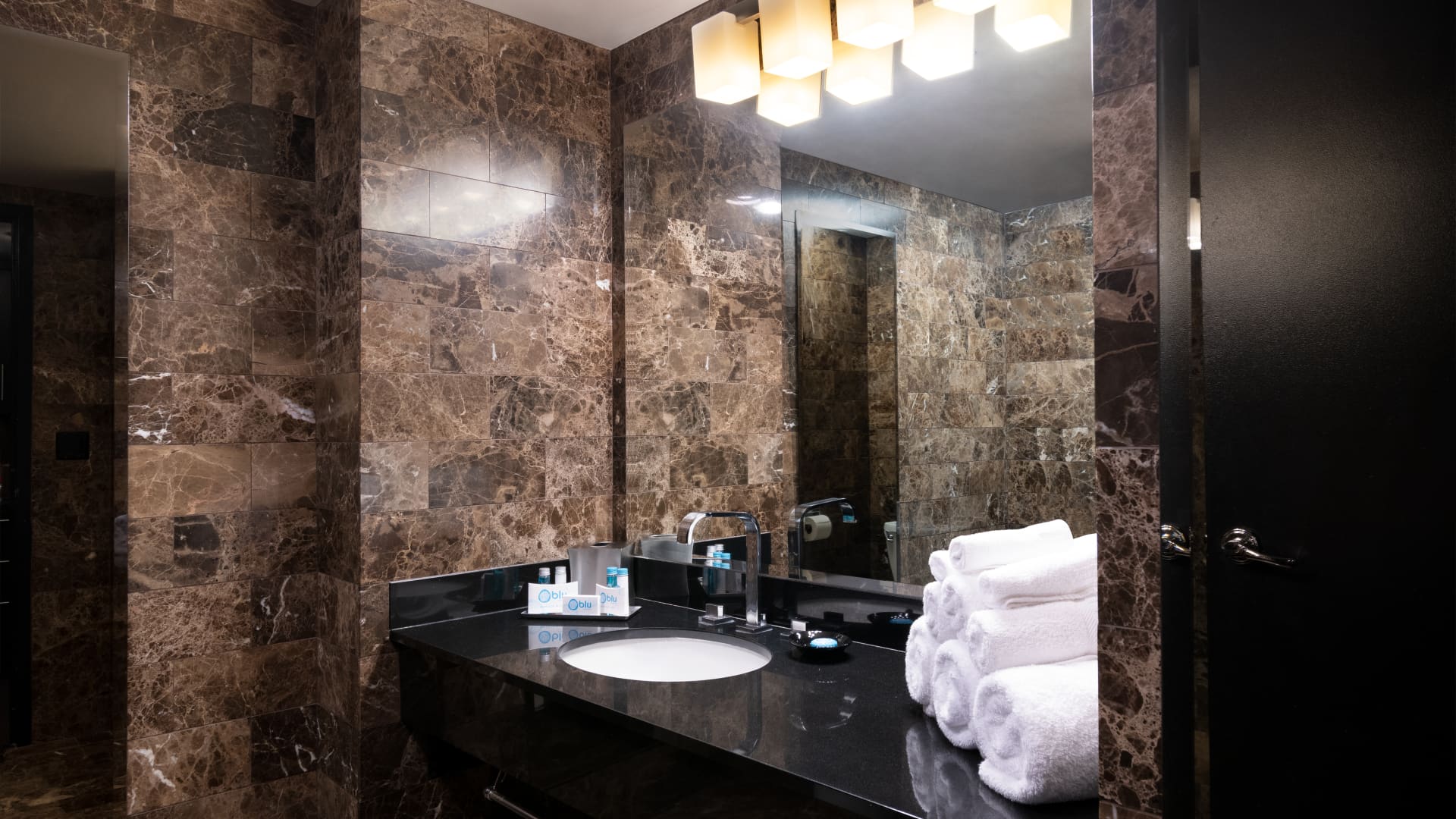 A bathroom sink with marble walls and countertops, a large mirror, and white towels.