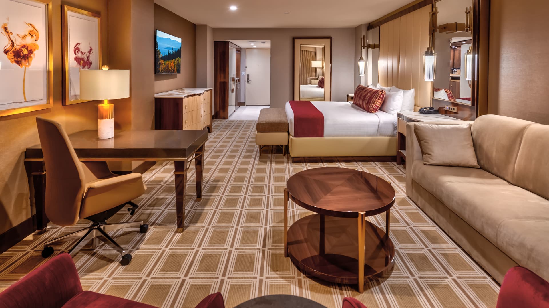 A wide view of a hotel room with a bed, sofa, desk, and TV.