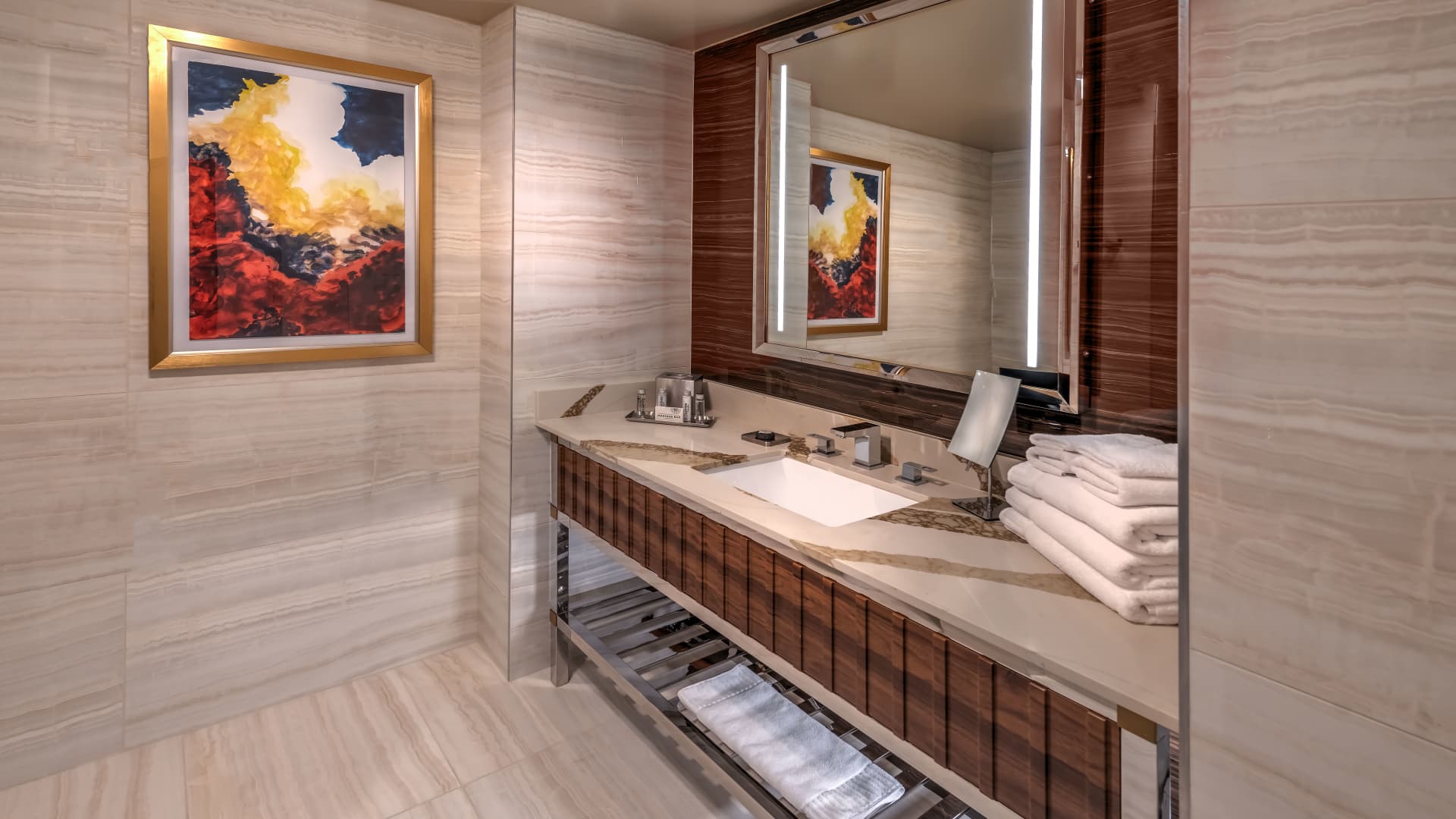 A bathroom sink area with a marble countertop, wooden cabinetry, and stacked towels.