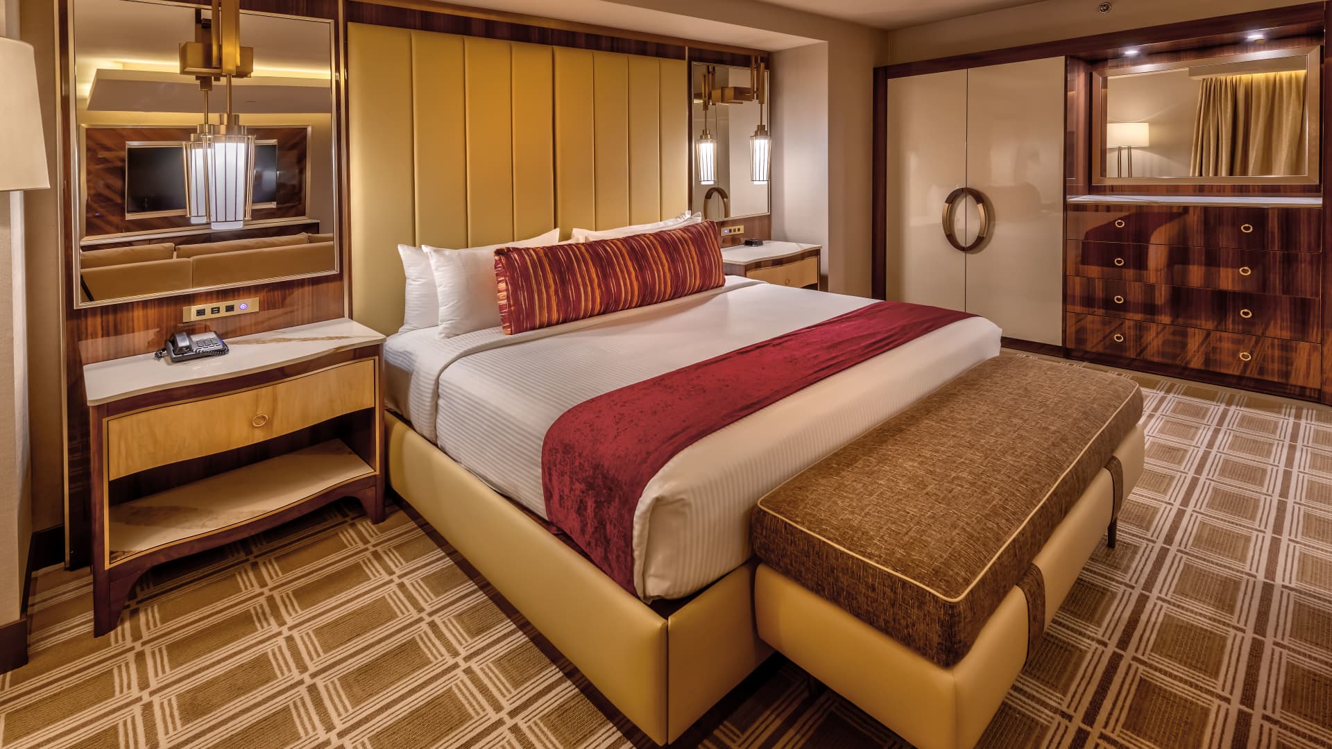 A luxurious hotel room with a large bed, desk, dresser, and bench.