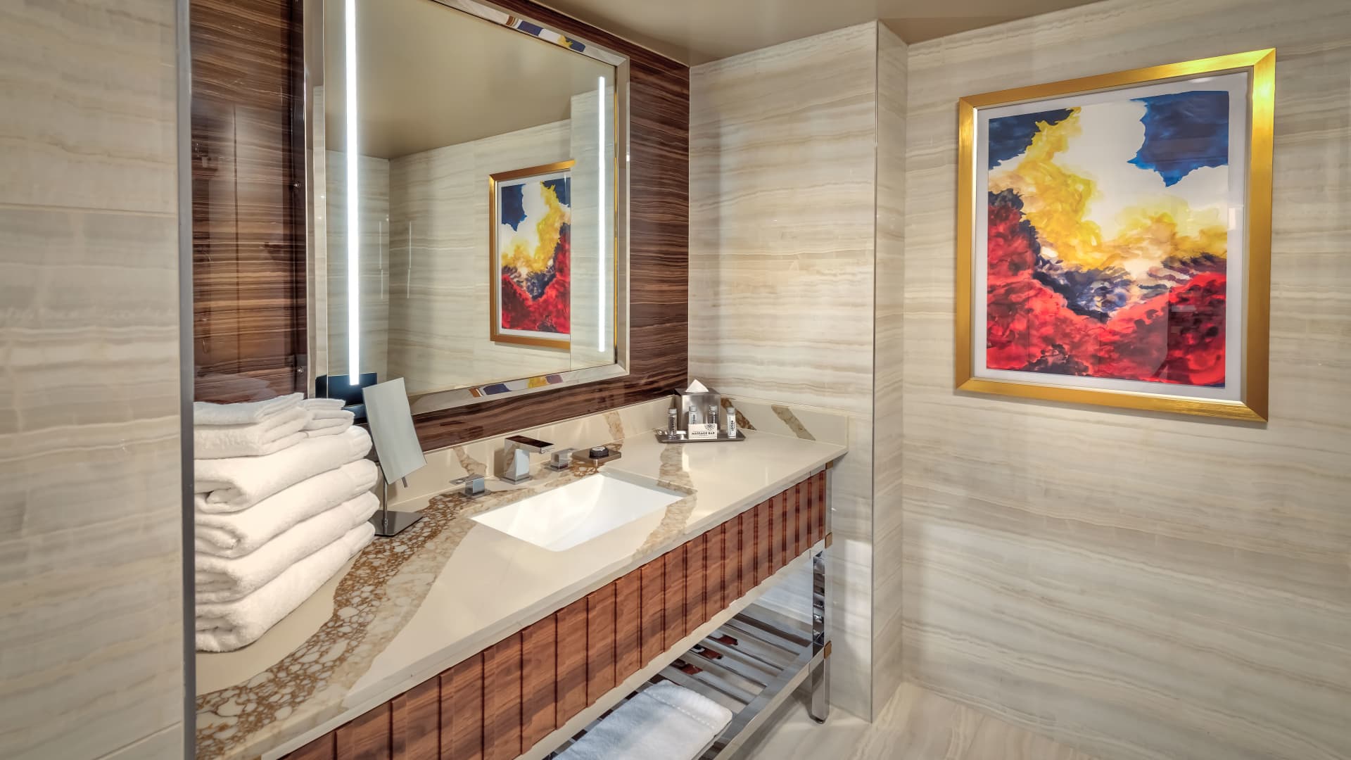 A bathroom with a marble tile wall, wood accents, a sink, and a stack of towels.