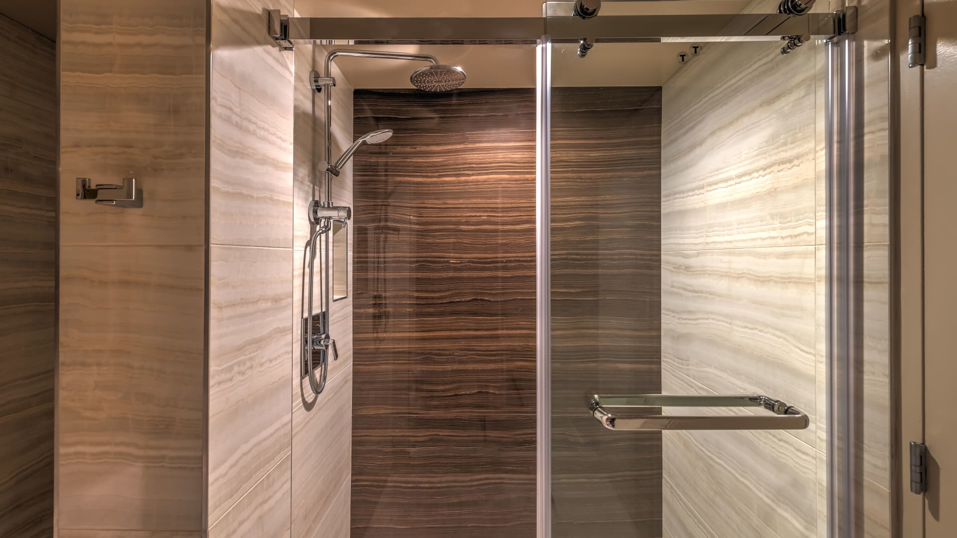 A modern shower with a glass door, marble tile, and a rainfall showerhead.