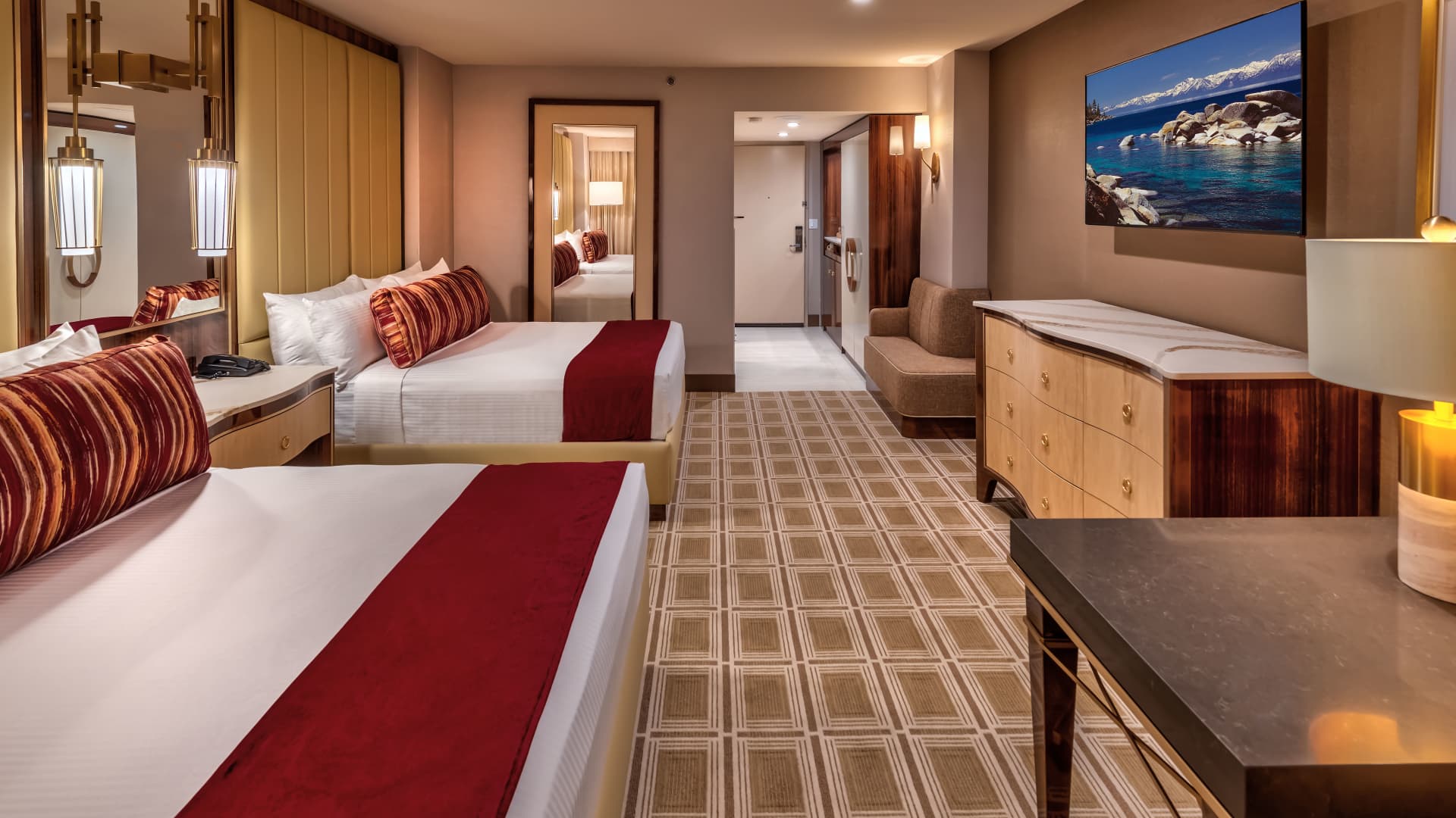 A hotel room with two beds, a dresser, a mirror, a TV, and a sofa.